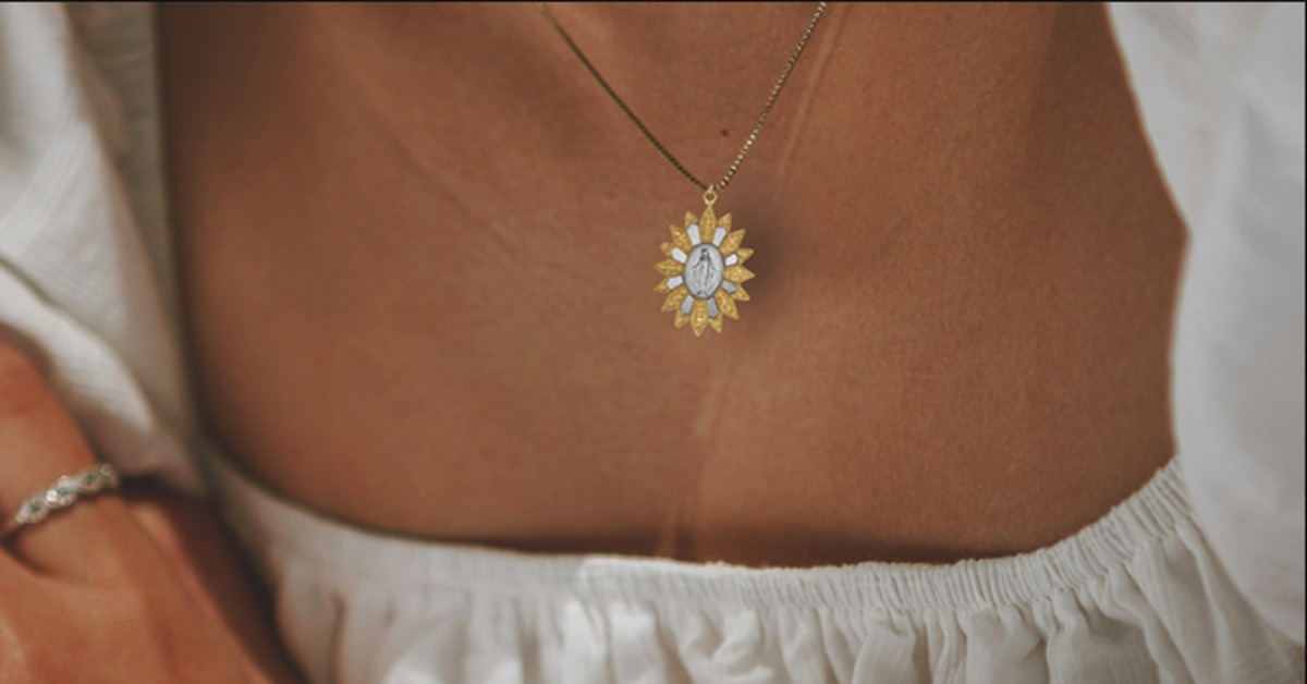 A person's neckline with a white blouse on and a religious necklace on. The pendant shows a Saint with a gold outline.