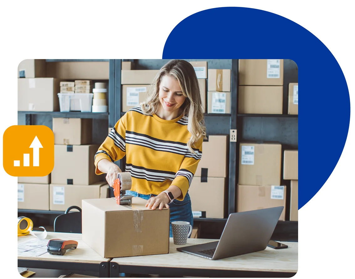 A woman engaged in packaging inside a warehouse, with various items and shelves arranged around her.